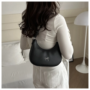 Minimalist black crescent shoulder bag with silver bow accent on matte leather texture