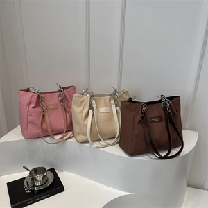 Three canvas tote bags in pink, beige, and brown with leather straps on a display stand