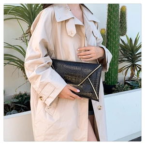 Detail of black crocodile texture envelope clutch bag with gold metallic edge accents