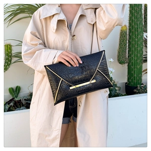 Detail of black crocodile texture envelope clutch with modern gold metal trim accent