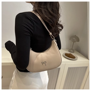 Detail of beige crescent underarm bag with silver bow ornament and leather texture