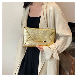 Glossy gold crocodile pattern envelope clutch bag with metal clasp shown in a hand