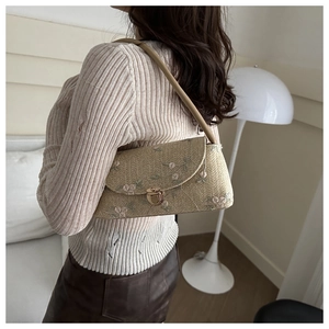 Detail of woven beige shoulder bag with floral embroidery and gold metal clasp