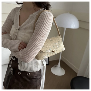 Detail of floral embroidery and metallic lock on a beige woven straw shoulder bag