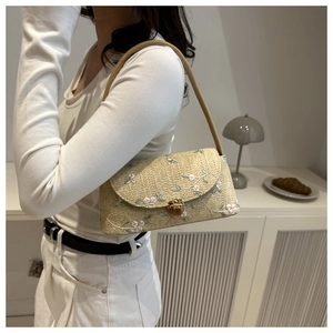 Detail of woven straw shoulder bag featuring floral embroidery and a gold turn-lock closure
