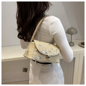 Detail of woven straw bag featuring floral embroidery and gold metal buckle on model