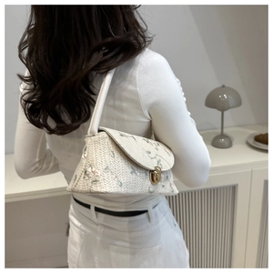 Model wearing a beige woven shoulder bag with floral embroidery and gold turn-lock