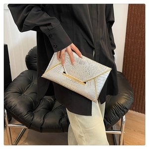Detail of silver crocodile-embossed clutch bag featuring elegant gold metal trim accents