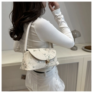 Close-up of woven straw shoulder bag featuring floral embroidery and gold metal lock