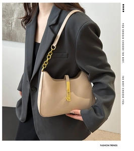 Detail view of beige leather underarm bag with gold lock and chain on grey blazer