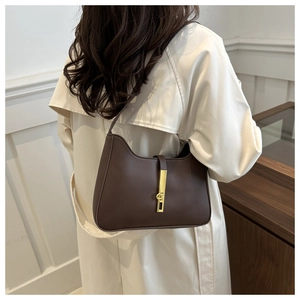 Detailed view of dark brown leather crescent bag with gold piston clasp on beige trench coat