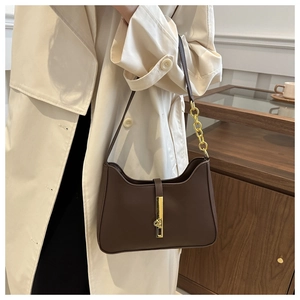 Détail d'un sac à bandoulière marron avec boucle dorée et chaîne sur un trench-coat beige