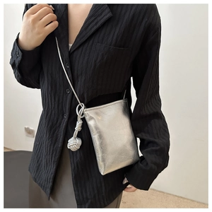 Close-up of a silver metallic crossbody phone bag with knot detail and textured finish