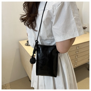 Minimalist black leather phone bag with a decorative woven knot detail on shoulder strap