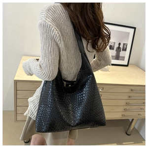 Detail of the black woven texture and polished leather strap on this large shoulder bag