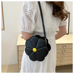 Detail of creative black daisy shoulder bag with yellow center on white lace dress