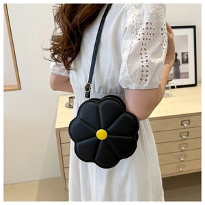 Détail d'un sac bandoulière noir en forme de fleur avec centre jaune sur robe blanche