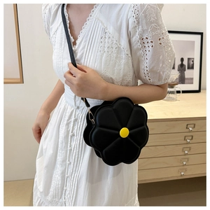 Detailed view of a black flower-shaped crossbody bag featuring a yellow center on white dress