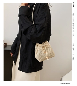 Side view of beige straw bucket bag with drawstring and gold bead tassel details
