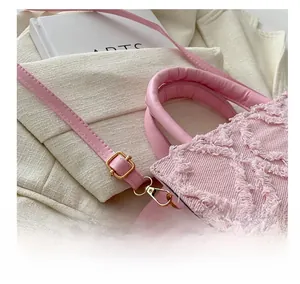 Close-up of pink denim handbag featuring quilted fringe texture and golden metal buckle