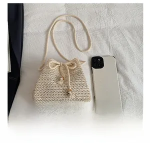 Detail of woven straw bucket bag with drawstring tassels and bead accents on white fabric