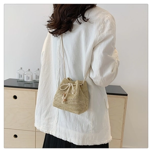 Detailed back view of a beige hand-woven straw bucket bag with drawstring and thin shoulder strap