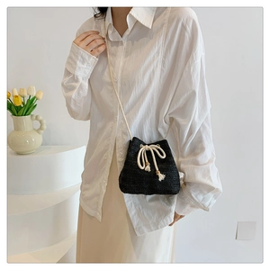 Detail of a black woven straw bucket bag with cotton rope drawstring and tassels