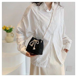 Detail of black woven straw bucket bag with white drawstring bow and tassel accent