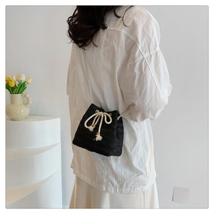Detail of black woven straw bucket bag featuring white drawstring with wooden beads