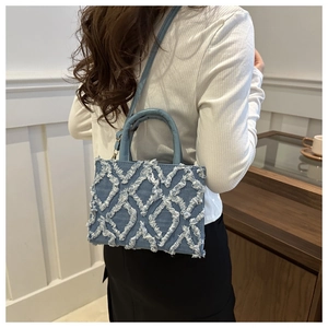 Detail of blue denim shoulder bag with white frayed fringe rhombic pattern and strap
