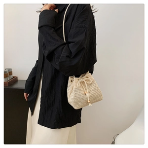 Detailed view of woven texture and drawstring closure on cream straw bucket bag