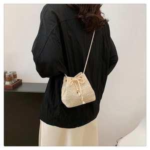 Straw bucket bag with drawstring closure shown on shoulder for beach fashion