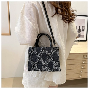 Detail of dark denim quilted bag with frayed fringe edges and black leather handle