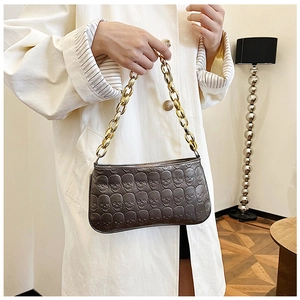 Detailed view of grey shoulder bag with embossed skulls and chunky gold chain strap