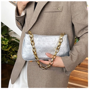 Detail of silver skull embossed handbag with chunky gold chain strap worn with blazer