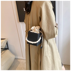 Detail of black bucket bag with pearl handle and gold chain strap on trench coat