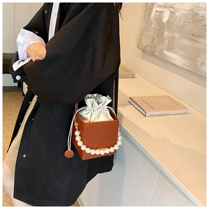 Detail of brown bucket bag featuring large pearl handle and drawstring closure