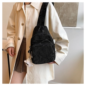 Detail of black pleated crossbody chest bag with plush doll charm and multi-pocket design