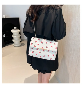 Close-up of white fabric shoulder bag with red strawberry print and gold chain strap