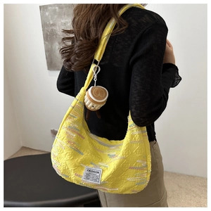Detail of yellow crescent shoulder bag featuring colorful stitching and plush coffee cup charm