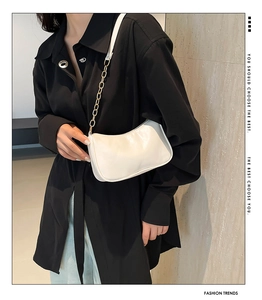 Detail of white square underarm bag with gold chain strap on a black outfit background