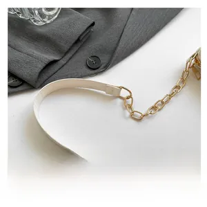 Detail of cream leather shoulder strap with gold chain links on a chic handbag