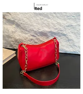 Detail of red vegan leather underarm bag with gold chain strap on a marble background