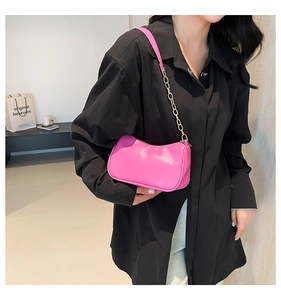 Detail of a bright pink leather underarm bag with gold chain strap shown on a model