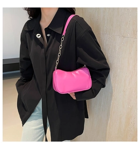 Detail of bright pink mini underarm bag with gold chain strap worn by a model