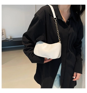 White glossy leather crescent shoulder bag with gold chain strap on model in black shirt