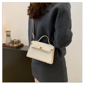 Detailed view of cream crocodile-embossed leather handbag with golden metal twist lock