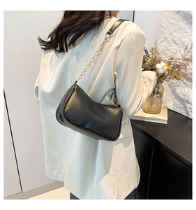 Detail view of black crescent moon shoulder bag with gold chain strap on ivory blazer