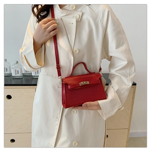 Detail of red crocodile pattern handbag with gold twist lock on a beige trench coat