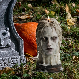 Spooky zombie head candle with glowing flame in outdoor Halloween graveyard setting